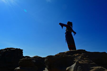 A woman standing with arms on a rocky hill (Silhouette photography)の写真素材