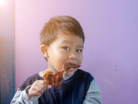 asian boy eating roasted chicken wing.の写真素材