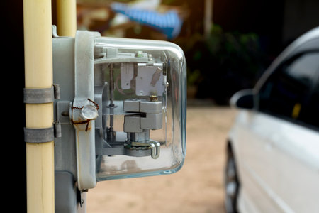 Front view of Power meter of Thailand attached to outdoor power pole. with yellow pipe beside of volt meter. and blurred of car parking on the ground.の写真素材