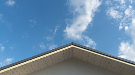 Gable corner of the roof of the central house used metal cheese roof. Under blue sky and white clouds.の写真素材
