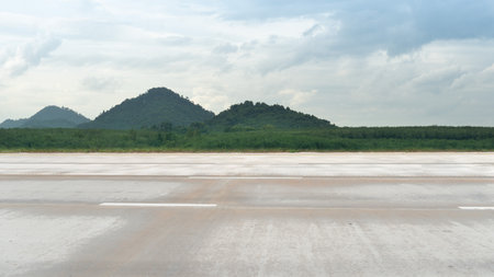 Horizontal view of empty concrete road with dust and grass. Background of green forest and mountain under tha sky with clouds.の写真素材