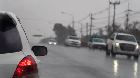 Rainy day scene with cars driving on a wet road. Foreground features a portion of a white car with a...