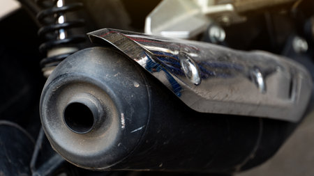 Motorcycle exhaust pipe. Pipe is primarily black with a chrome or silver heat shield. Focus is on the exhaust end and the metallic shield highlighting the texture.の写真素材