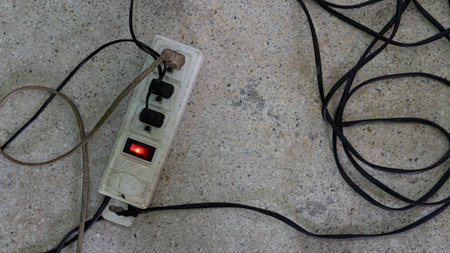 An old electrical outlet lying on the concrete floor. All three sockets are working. Wires are strung together and not aesthetically pleasing.の写真素材