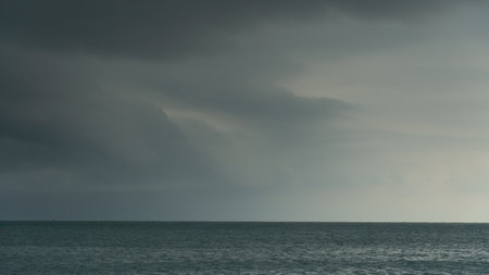 Vast expanse blue water of ocean under a cloudy overcast sky. Horizon line is visible with faint landmasses in the distance. The scene is moody and atmospheric before heavy rain.の写真素材