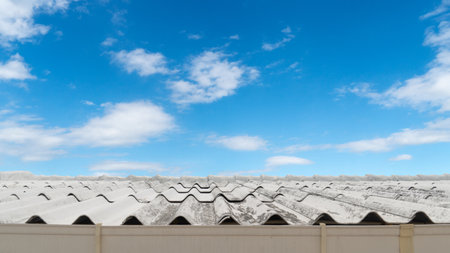 Roof of the house is made of normal colored tiles and has been used for a long time. In front, there is a PVC gutter to drain rainwater. Under blue sky and white clouds.の写真素材