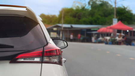 Rear side of white car driving on the road. Clear traffic in rural areas. Background of Small village in Thailand and green forest under the sky.の写真素材