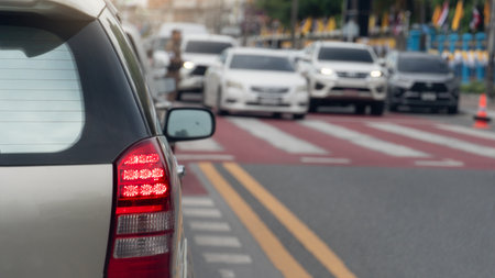 Rear side of gold car with turn on brake light. Car on the opposite side stops on the green light to allow people on the crosswalk to cross the road.の写真素材