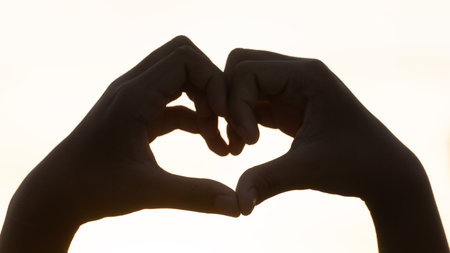 Hands creating a heart shape against a bright background, silhouetted by the light. This image evokes feelings of love romance and care. Perfect for Valentine's Day.の写真素材