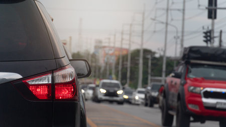 Rear side of black car on the road with turn on brake light. Several cars were passing through the intersection from the opposite side. Blurred of electric poles line the roadside.の写真素材