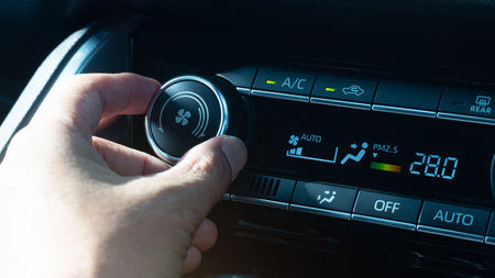 Man hand adjusting the temperature of a car climate control panel. Control panel has a digital...