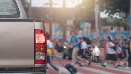 Rear side of car with turn on brake light on the road. Road crossing point with blurry image of students passing by.  Stop to pass for safety reasons. Morning time in the city of Tの写真素材