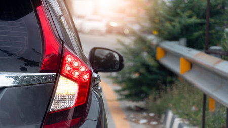Rear side of grey car close up taillight on the road. Traffic barrier with grass and trees growing...