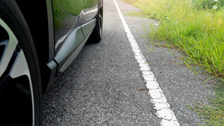 Car parking on the road with white line on the side of the road. Sides of the road are densely lush...