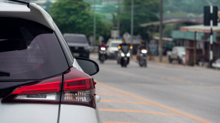 Rear side of white car driving on aspahlt road. Road with yellow for seperate road. There are cars and motorcycles driving past the opposite lane.の写真素材