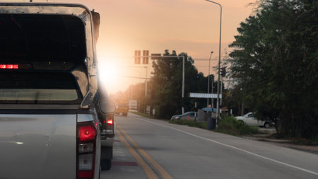 Rear side of transport pickup car silver color with turn on brake light. All cars are stopped at the traffic light ahead at the intersection. Light shining against the evening sky.の写真素材