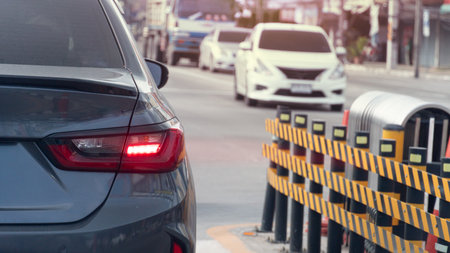Rear side of grey car with turn on brake light. Front of car stuck in traffic at an intersection. Side of the road barrier is made of steel and has a strip. Cars are heading past in front.の写真素材