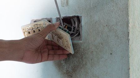 Hand of maintenance people use screwdriver unplug light switch. Socket of switch and power plug take...