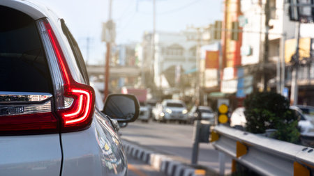 Rear side of luxury white car with trun on brake light. Stop on the junction from traffic light control. Opposite raod with many cars queue up. Blurred of town at day time.の写真素材