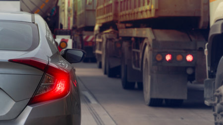 Rear side of sedan grey color with turn on brake light. Stop and queue on concrete road. Surrounded by big trucks in business time.の写真素材