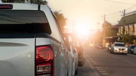 Side of pickup car parking beside road. Dim light of a warm evening. Other car driving on clear road. City and buildings along the road. Under light and evening sky.の写真素材