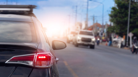 Rear side of black car with turn on brake light. Close up tail light of car with bright light of the brake lights. Blurred of other car on opposite road. With environment of city.の写真素材
