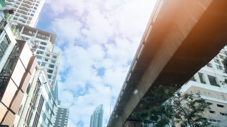 Low angle view of modern skyscrapers and BTS Skytrain tracks in Bangkok under a blue sky with white...