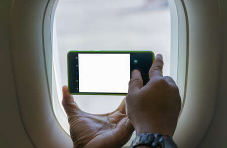 Holding a smartphone with a blank screen to take pictures by the window on an airplaneの写真素材