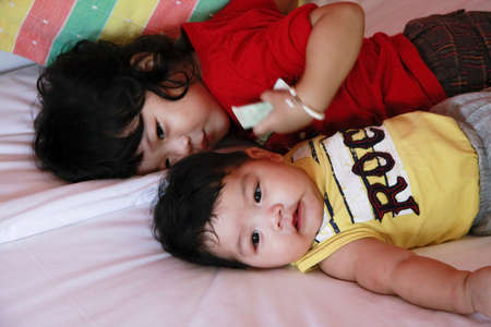 Sister in Red suit and Young Brother in Yellow suit on the bed の写真素材