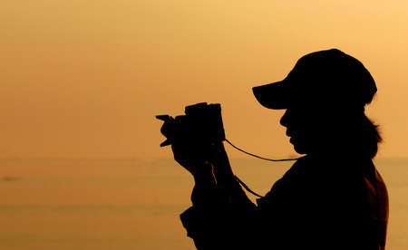 Woman is shooting Photo Sky is Orange at Sunset Backlight make Silhouette  の写真素材