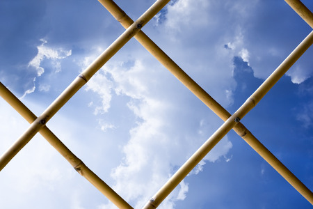 Expand white cloud on blue sky see thru bamboo fence.Bright sunlight from left side.の写真素材