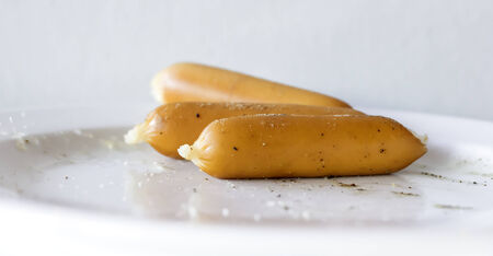 Three hotdog on white plate.Some pepper and salt spread over on hotdog and plate.Only in focus at one hotdog in front.の写真素材