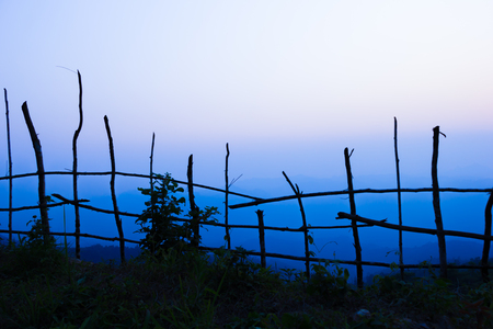 Dark tree and fence stick in shadow at foreground.Mountain at background.Sun nearly go down.の写真素材