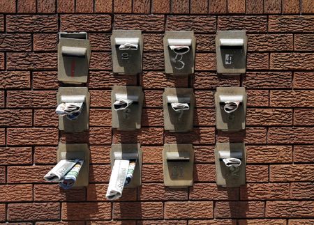 Twelve Mailboxes With Newspapers Inside On A Red Brick Wall