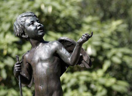 Young Angel Statue, Dark Metal Sculpture In Front Of Green Plants, Sydney Public Parkの写真素材