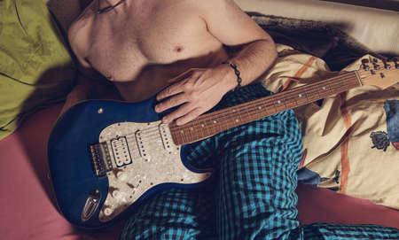 Man in pajamas holding guitar in bedの写真素材
