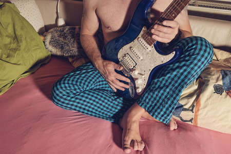 Man in pajamas holding guitar in bedの写真素材
