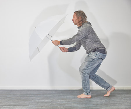 Man with white umbrella in front of a white wallの写真素材