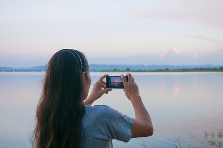 Female taking photo the sky and water in morning light.の写真素材
