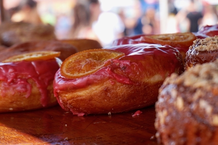 Gooey donuts on display with pink frosting & candied orange. Sitting in the shade, on display for sale outdoors.の写真素材