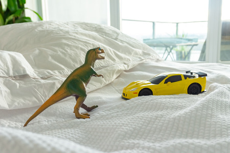 Toy dinosaur and car on parent's bed, depicting family home and parenting life. White linens in background.の写真素材