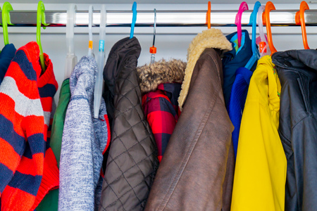 Little boy's child size jackets, coats and sweaters hanging in a kid's closet with colorful hangers.