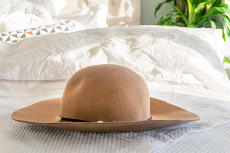 Woman's beige sun hat with trim and wide brim on a fluffy bed, with sunlight shining indoors. Depicting holidays, relaxation and going out in fashion.の写真素材