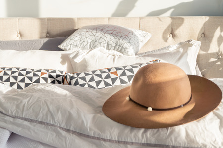 Woman's beige sun hat with trim and wide brim on a fluffy bed, with sunlight shining indoors. Depicting holidays, relaxation and going out in fashion.の写真素材