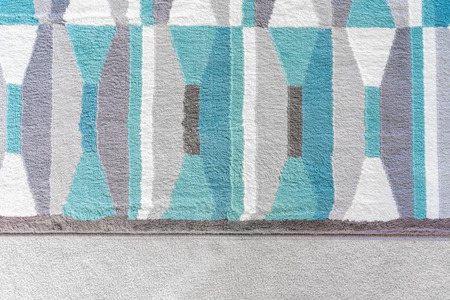 Background graphic, top view of a geometric rug with blue and grey color patterns, on top of a beige carpet, as a design element in home decor.の写真素材