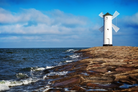 White old lighthouse in Swinoujscie, stone pier and wavy sea, Polandの写真素材