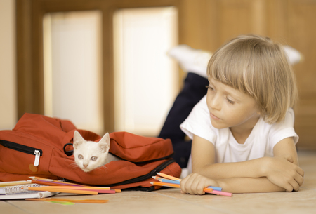 Back to school. Kid getting ready for classes packing backpack with stationary and white catの写真素材