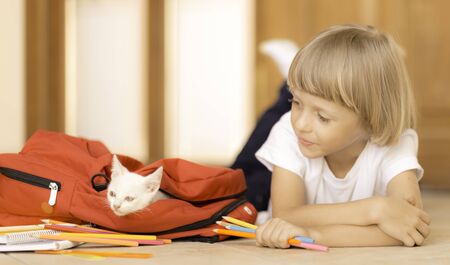 Back to school. Kid getting ready for classes packing backpack with stationary and white catの写真素材