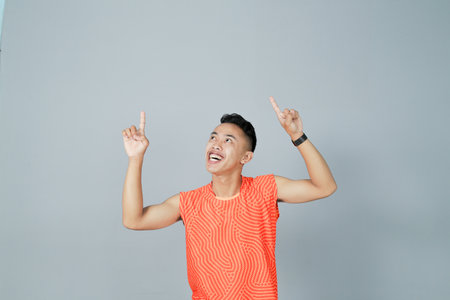 a young man wearing a orange shirt is showing something happily, isolated on a gray background