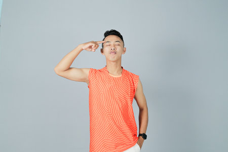 a young man wearing an orange shirt is showing a gesture of enthusiasm, isolated on a gray backgroundの写真素材